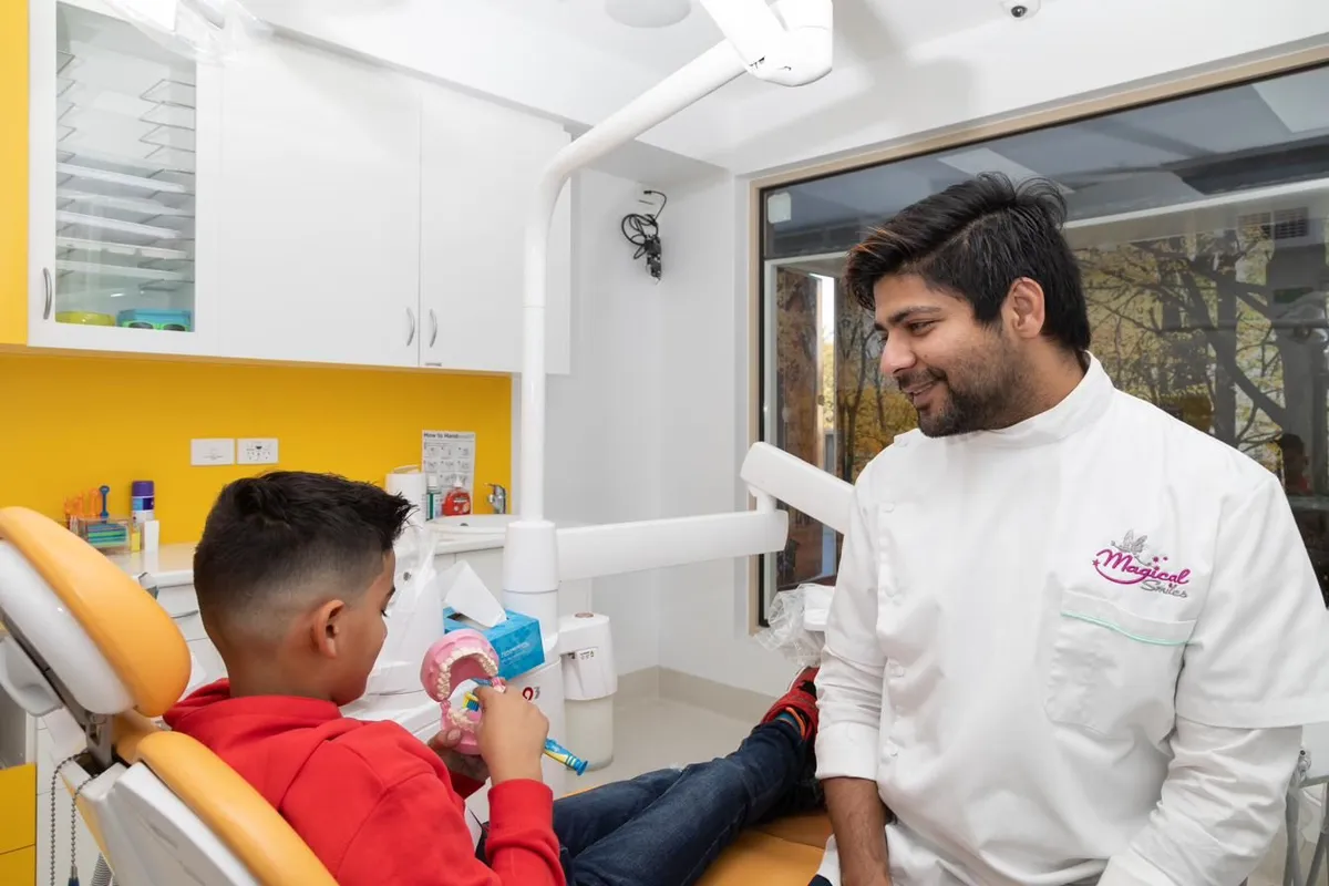 A child in the dental chair being shown a colourful teeth model by a clinician in a Magical Smiles uniform — show-and-tell before any treatment begins.