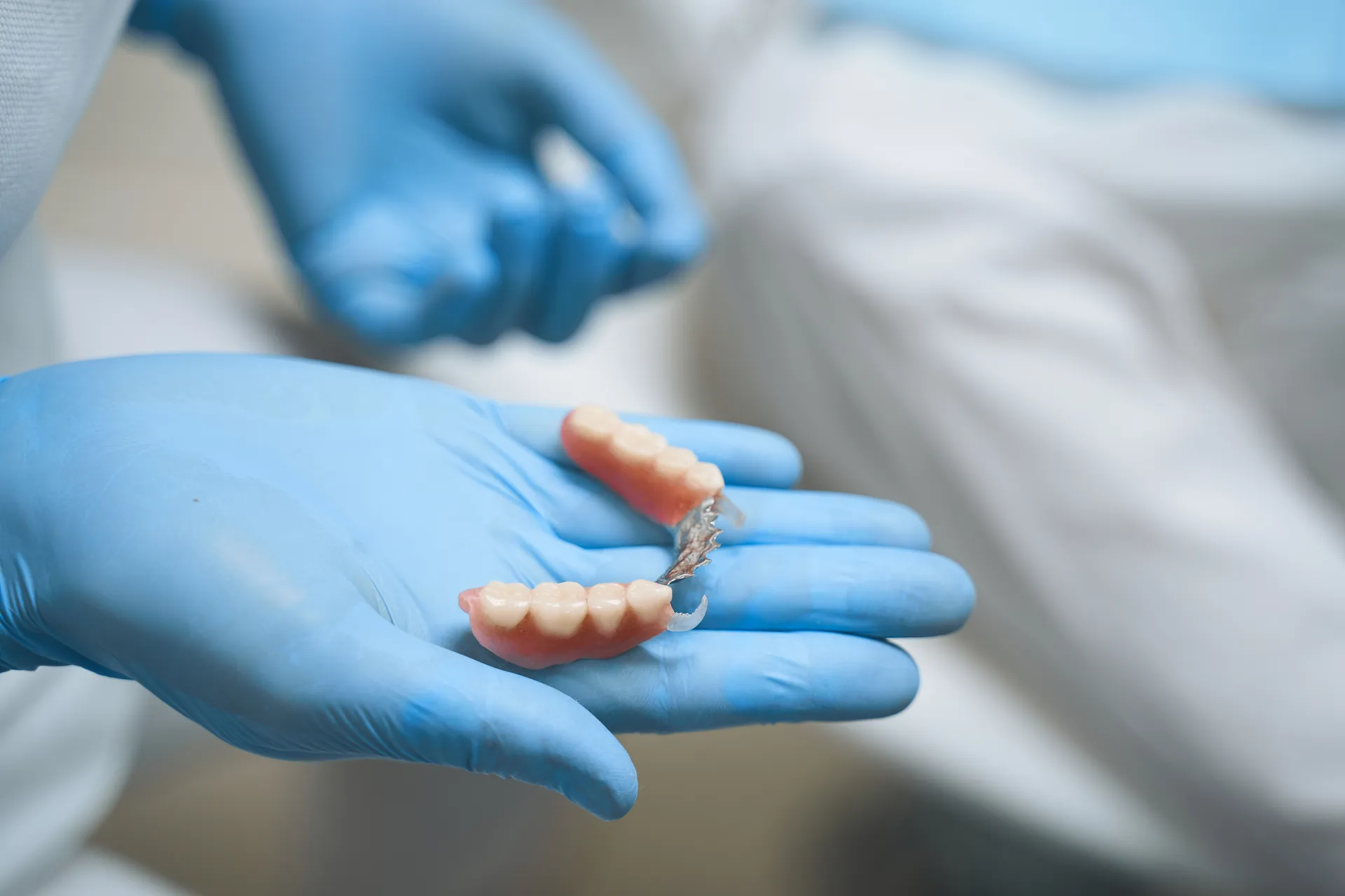 A dentist holding a dental prosthetic in gloved hands