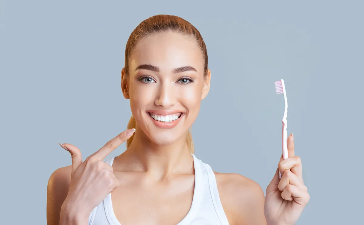 A woman pointing to her teeth while holding a toothbrush