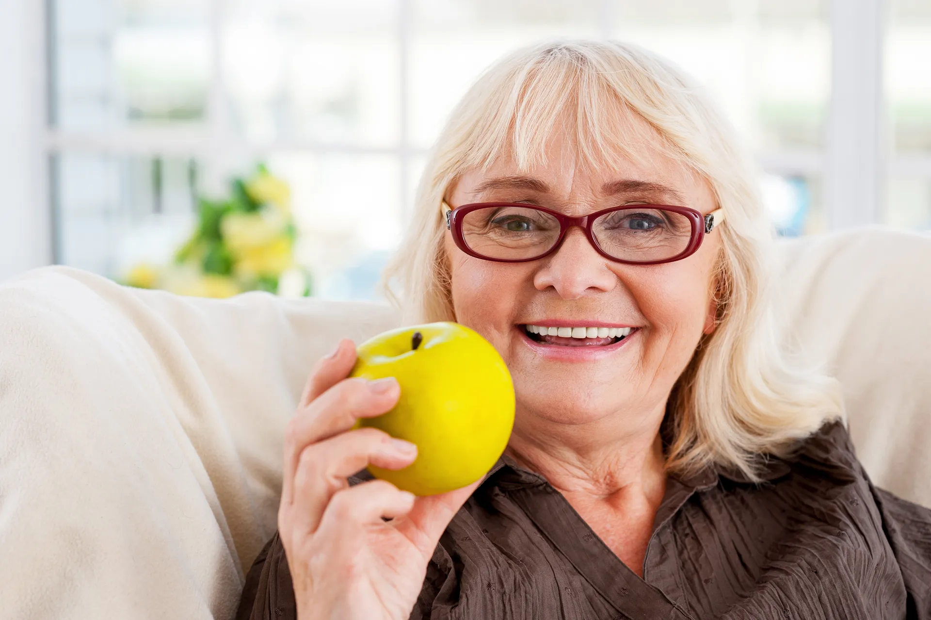 A smiling senior woman comfortably holding an apple, enjoying everyday foods again