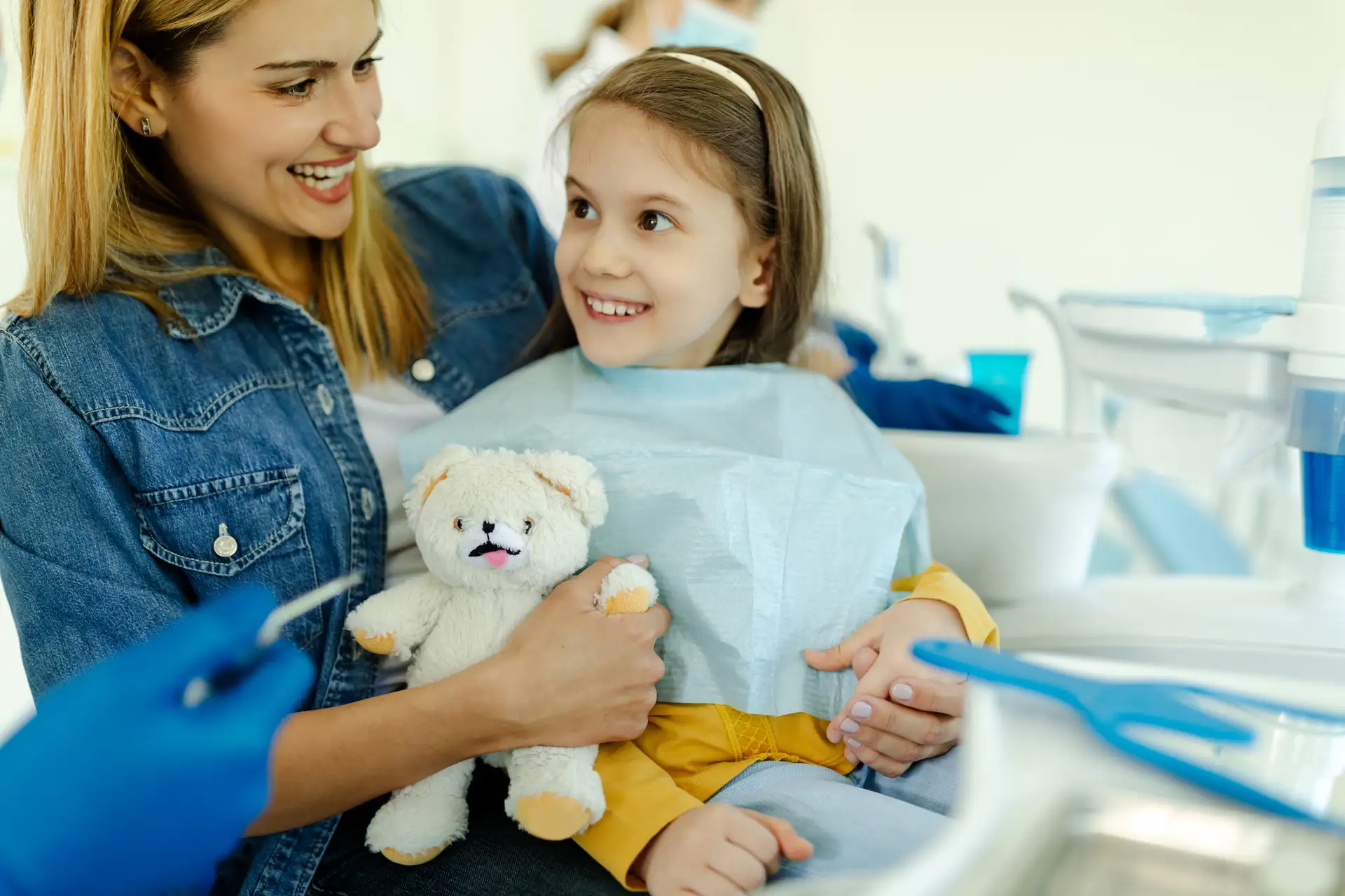 Young child smiling happily in the dental chair with her teddy bear