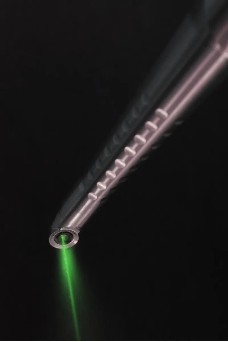 Close-up of the silver titanium laser handpiece body with green beam emerging from the tip
