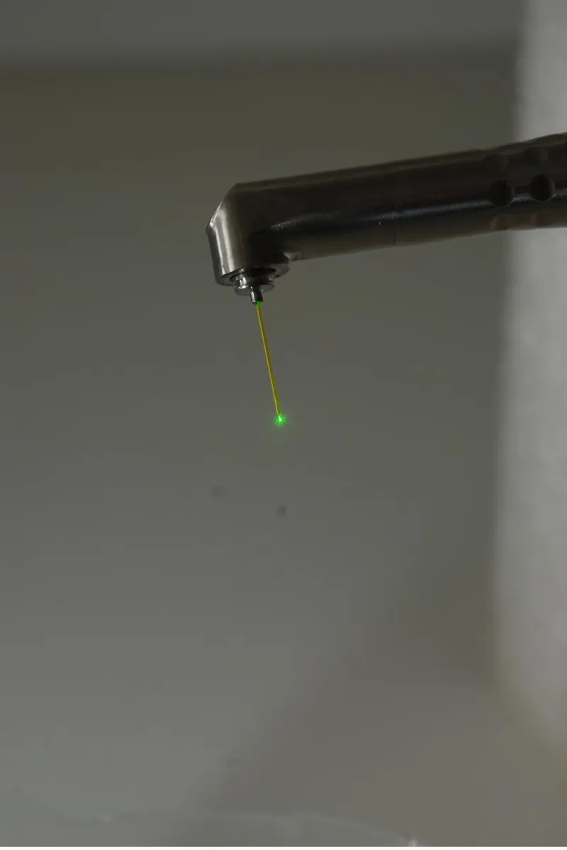 Wider angle of the Fotona dental laser handpiece showing the visible aiming beam used during ceramic debonding