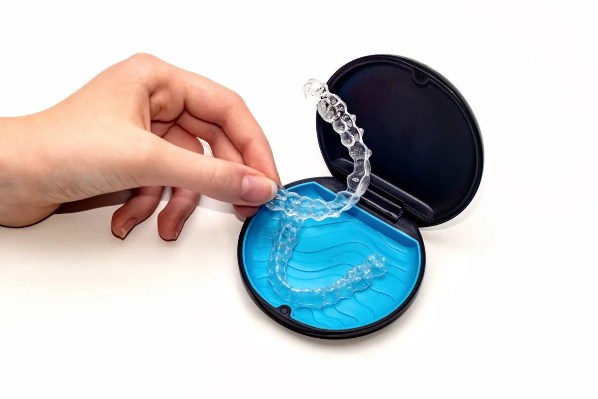 A clear aligner tray held beside its travel storage case